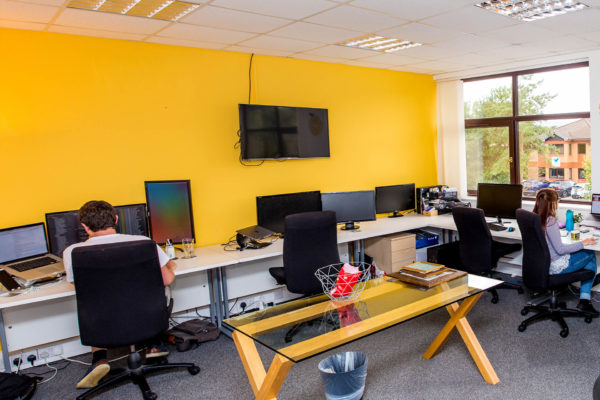 Yellow office space with desks, computers, monitors and employees situated within entrepreneurial hub, Welsh ICE.